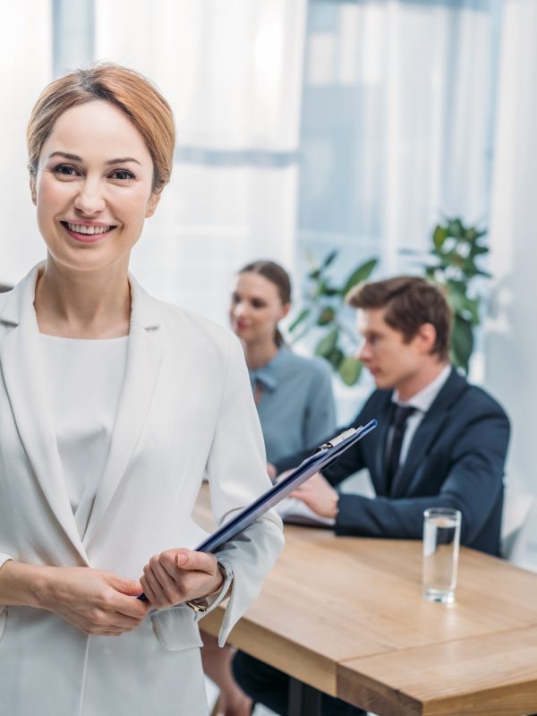 selective-focus-of-cheerful-recruiter-standing-with-clipboard-near-coworkers.jpg